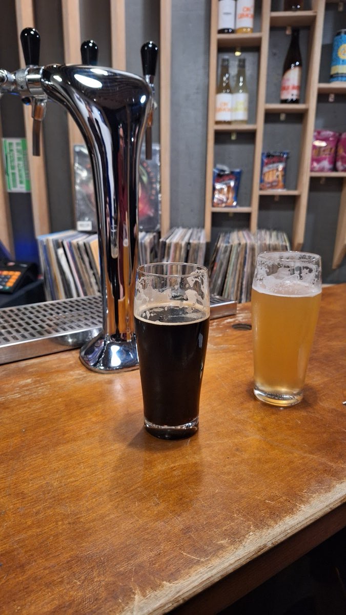 Ciemny stout i mętne jasne piwo w szklankach na drewnianym barze, obok chromowana kolumna kranów